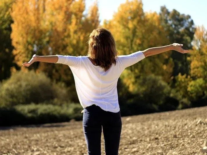 Frau mit ausgebreiteten Armen auf einem Feld im Herbstlicht
