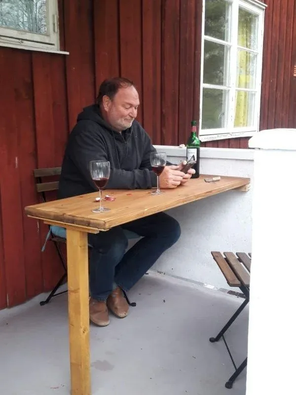 Mann sitzt an einem Holztisch vor einer roten Hauswand