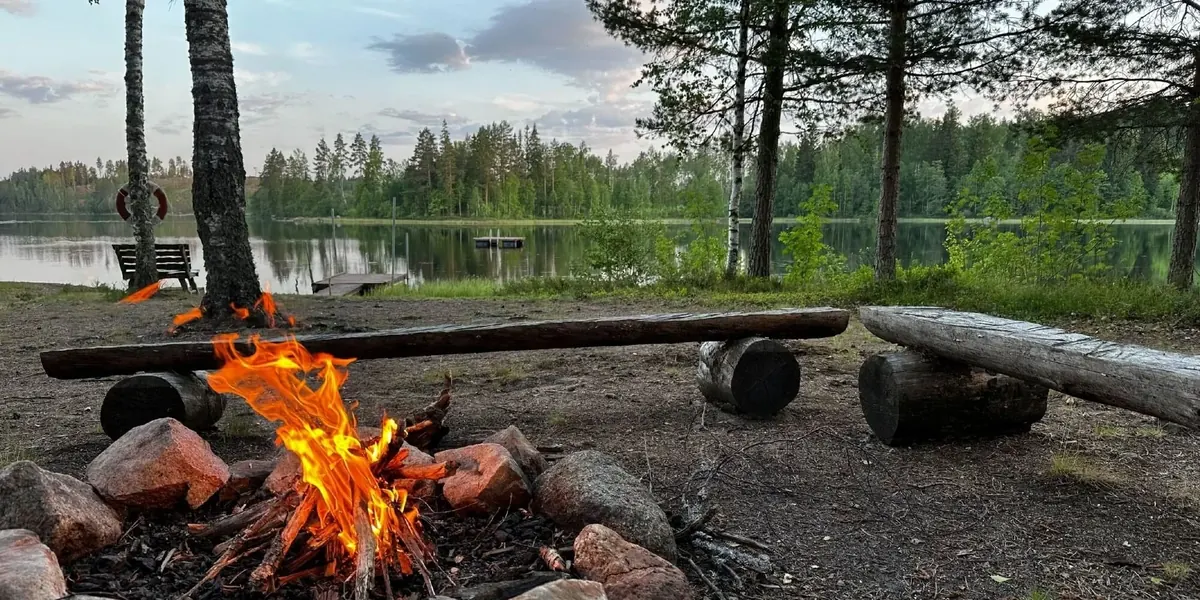 Lagerfeuer am Seeufer unter Kiefern