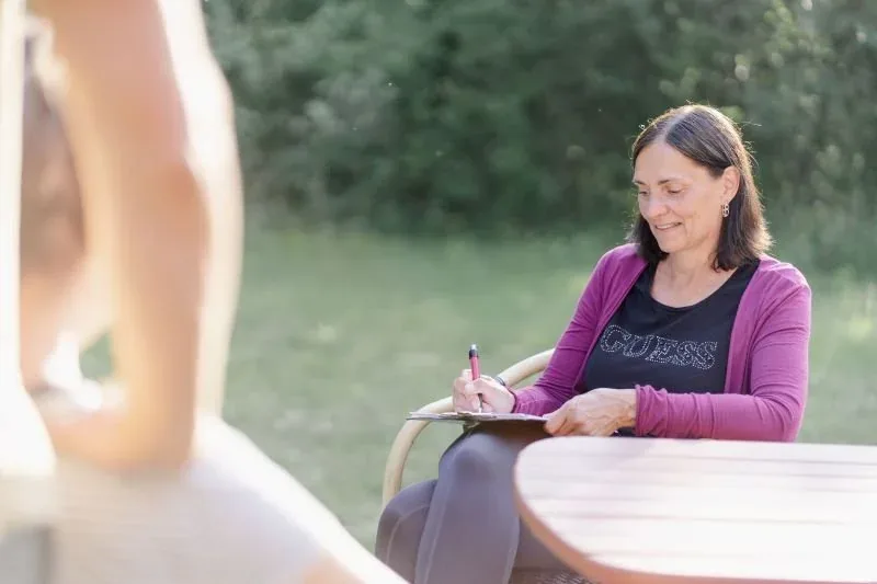 Nicole schreibt am Gartentisch in ein Notizbuch