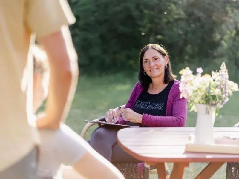 Frau lächelt am Gartentisch mit Blumenstrauß