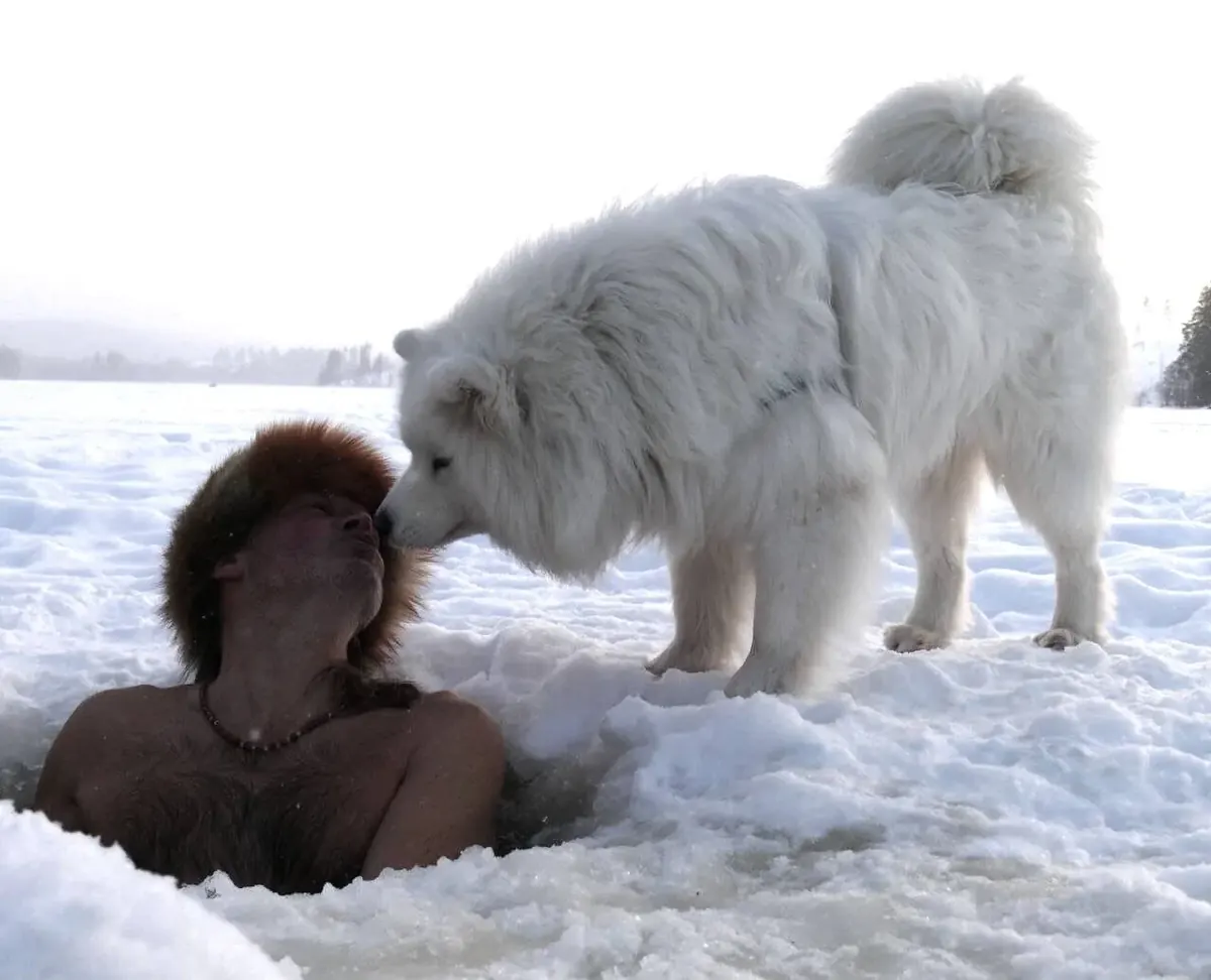 Frau im Eisloch und ein weißer Hund im Schnee