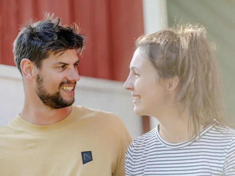 Ein Mann und eine Frau lachen vor einer roten Hauswand