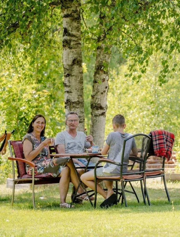 Gäste und Gastgeber sitzen in Gartenstühlen unter Birken