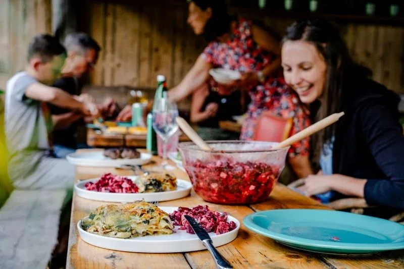 Gäste beim gemeinsamen Essen an einem Holztisch mit bunten Salaten