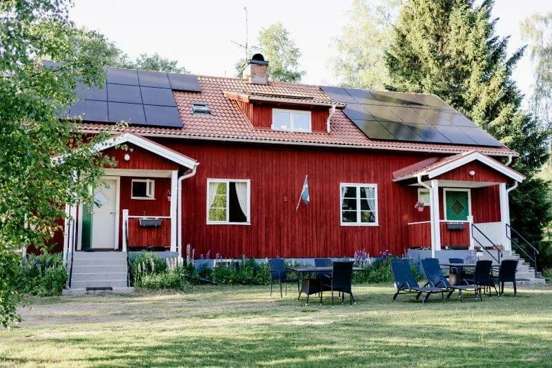 Rotes Schwedenhaus mit Solarmodulen, davor ein Garten mit Sitzgruppe