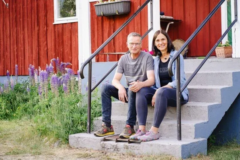 Nicole und Rainer sitzen auf der Treppe vor dem roten Haus, daneben blühen Lupinen
