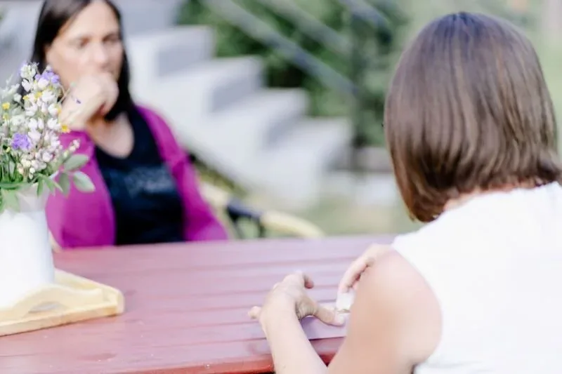 Zwei Frauen im Gespräch an einem Tisch mit Blumen